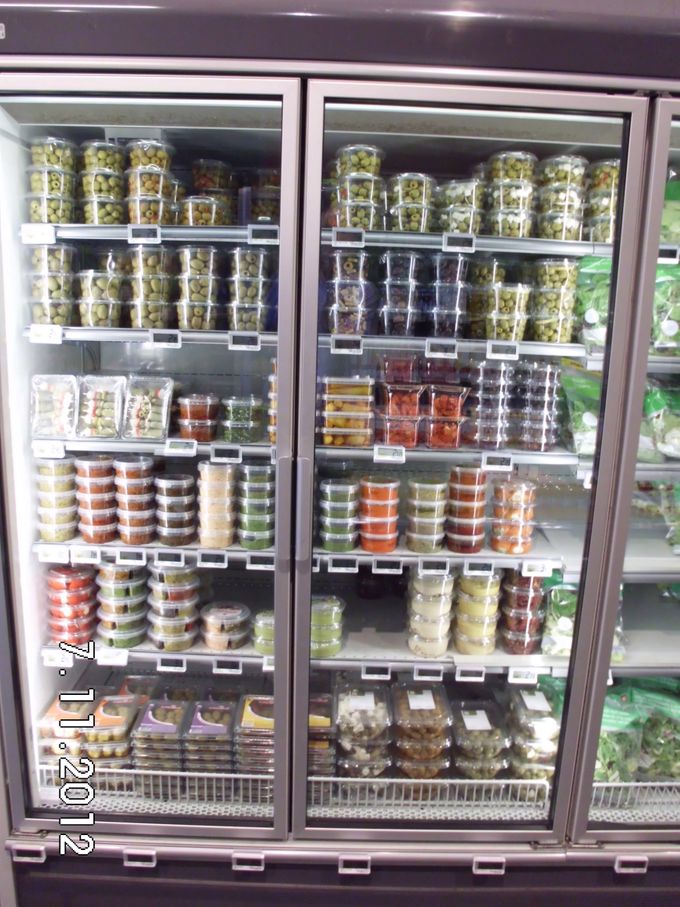 Mooi en verzorgd assortiment olijven, tapenades , gedroogde en gemarineerde tomaatjes voorverpakt in gesloten wandkoeling in supermarkt.